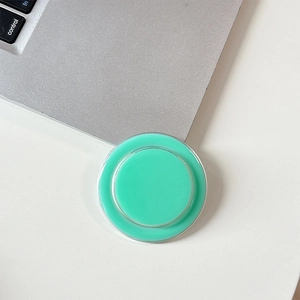 Detail view of mint green circular MagSafe phone stand next to a laptop on white desk