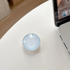 Detailed view of a light blue round crystal glass pop socket on a clean white desk