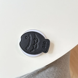 Macro shot of black fish-shaped leather phone grip with detailed lychee texture and embossing