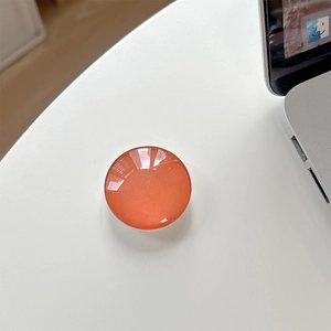 Detail view of glossy orange crystal glass phone grip on a white office desk surface