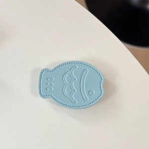 Detail of light blue fish-shaped leather phone grip with embossed cartoon face and stitching