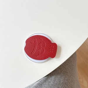 Macro view of red leather fish-shaped phone grip with lychee texture and fine stitching