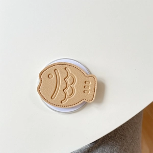 Detailed view of fish-shaped leather phone grip with scale texture on a white surface