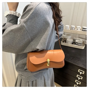 Brown leather shoulder bag with a gold metal clasp shown on a model in home setting
