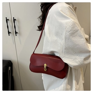 Detail of burgundy leather shoulder bag with a gold U-shaped buckle and fine strap