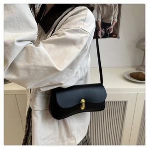 Close-up of black leather shoulder bag with gold oval clasp worn by a model