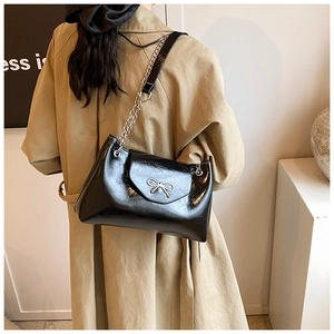Detail of glossy black shoulder bag featuring a silver bow buckle and chain strap