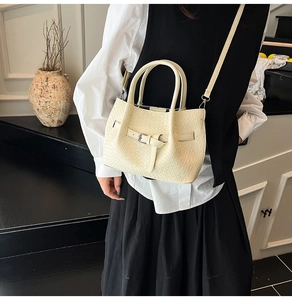Detail of cream bucket bag showing woven texture, silver buckle, and slim shoulder strap