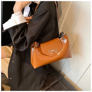 Close-up of brown glossy leather shoulder bag featuring a metallic bow clasp and chain strap