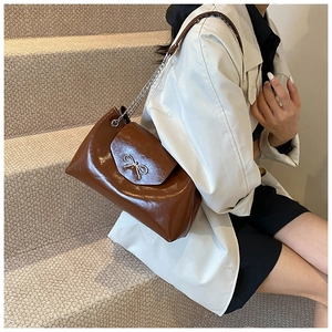 Detail of a brown glossy tote bag featuring a silver bow buckle and metal chain strap