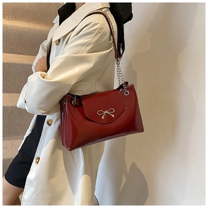 Detail of burgundy patent leather shoulder bag with silver bow accent and chain strap