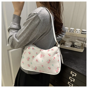 Close-up of white underarm bag featuring pink rose clusters and bow patterns worn on shoulder
