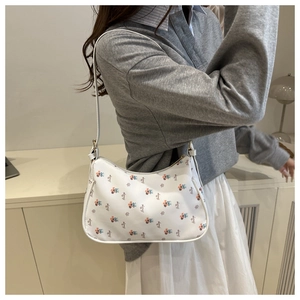 Close-up of white underarm bag with floral print and gold zipper detail on a shoulder