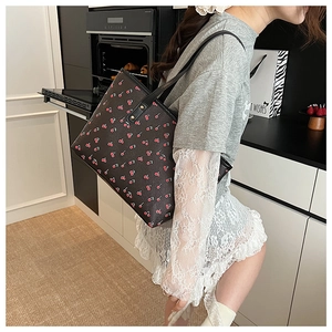 Close-up of black tote bag with red cherry prints and stylish side rivet details
