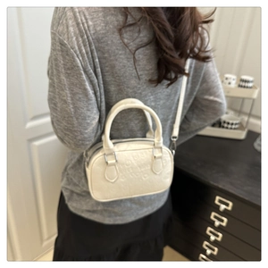 Detail of a creamy white embossed leather handbag shown worn on the shoulder by a model