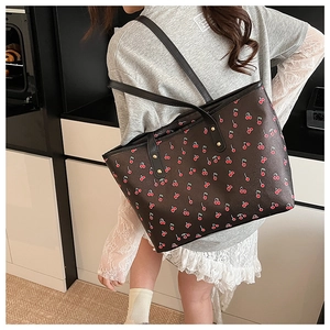 Detail view of large tote bag featuring red cherry print and gold rivet hardware