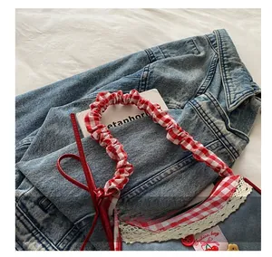 Detailed close-up of denim handbag featuring red gingham handles and lace cherry patch