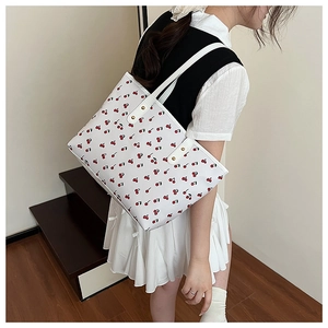 Detail of a large white tote bag with red cherry print and gold rivets on a shoulder strap