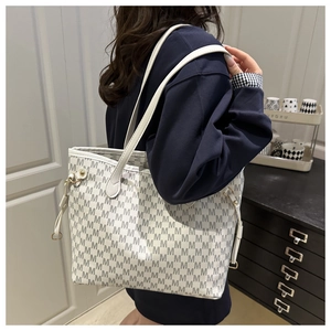 Detail of large white tote bag featuring gray letter patterns and gold hardware accents