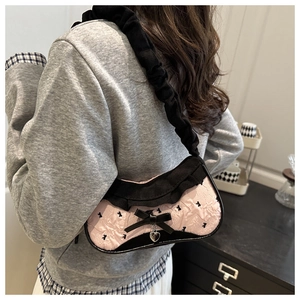 Detail of pink pleated underarm bag with black bow and heart pendant on shoulder