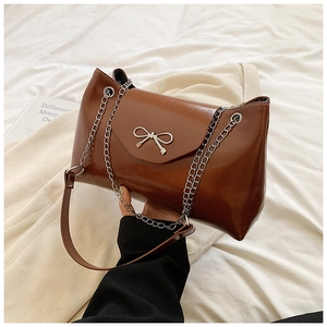 Brown patent leather tote bag with silver chain and bow buckle on warm textile background