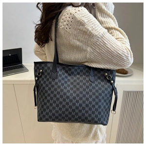 Detail view of a large black printed tote bag with M-pattern and slim leather shoulder straps