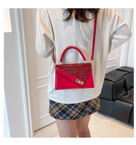 Détail du sac rouge à motif crocodile sur mannequin montrant le fermoir doré et la taille