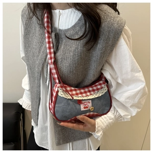 Detail of blue denim crossbody bag featuring red gingham trim and cherry embroidery