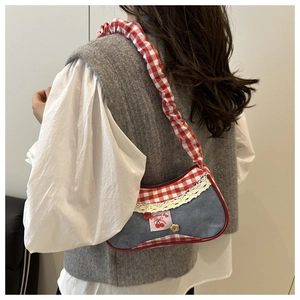 Detail of a denim shoulder bag featuring red plaid ruffles, lace trim and cherry embroidery
