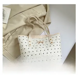 Detail of cream tote bag featuring embossed texture and golden metal bow decoration