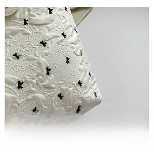 Macro shot of white textured tote bag fabric with black bow patterns and fine stitching