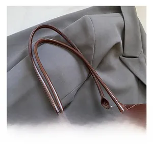 Detail of slim long handles and metallic logo on dark brown glossy leather shoulder bag