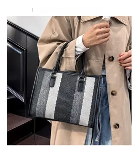 Detail of striped canvas tote bag with black leather handle and golden metal rings