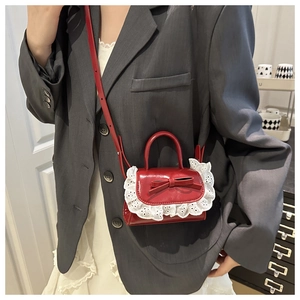 Detail of red bow handbag with white lace trim showing smooth leather texture and crossbody strap