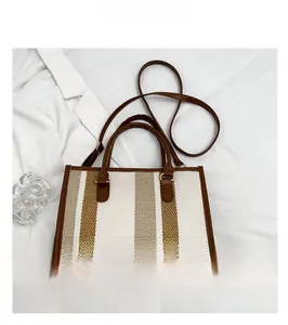 Flat lay of a striped tote bag with brown leather handles and gold-toned metal hardware