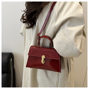 Detail of burgundy patent leather handbag with gold metal clasp on beige trench coat