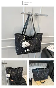 Detail of black tote bag with white bow patterns, featuring a golden pendant and plush charm
