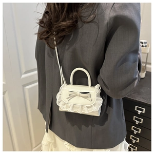 Close-up of beige mini crossbody bag featuring delicate lace ruffles and a leather bow