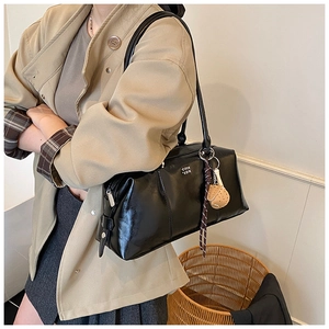 Detail of black glossy leather Boston bag with metal logo and ribbon charm accessory