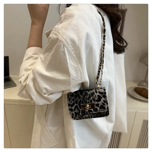Close-up of leopard print mini crossbody bag with gold chain strap on a white shirt