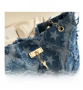 Détail du sac en jean bleu avec étoiles blanches, bords effilochés et breloque cerf dorée