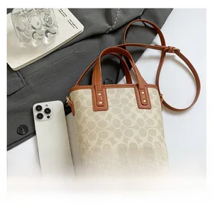 Detail der beigen Monogramm-Beuteltasche mit braunem Ledergriff und goldenen Nieten