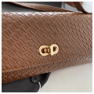 Detailed close-up of dark brown woven texture and gold metal twist lock on the handbag