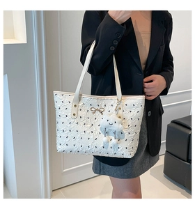 Detail of white tote bag with embossed texture, golden bow hardware and plush charm