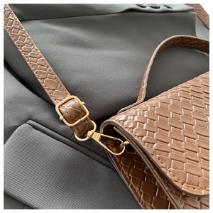 Close-up of brown woven leather texture with adjustable gold metal buckle on a shoulder bag