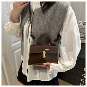 Detail shot of a vintage brown patent leather crossbody bag with a gold buckle clasp