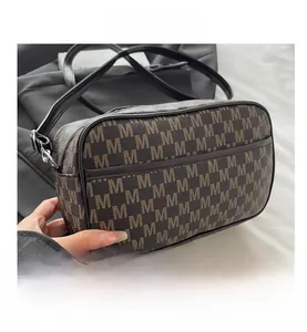Macro view of brown monogram crossbody bag showing detailed M-pattern and zipper closure