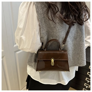 Detail of glossy brown patent leather shoulder bag with gold clasp and fine texture