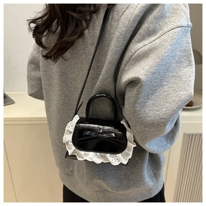 Detail of mini black crossbody bag with white lace trim and bow on a grey sweater