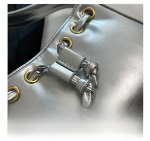 Macro view of metallic silver handbag featuring large gold eyelets and leather knot details